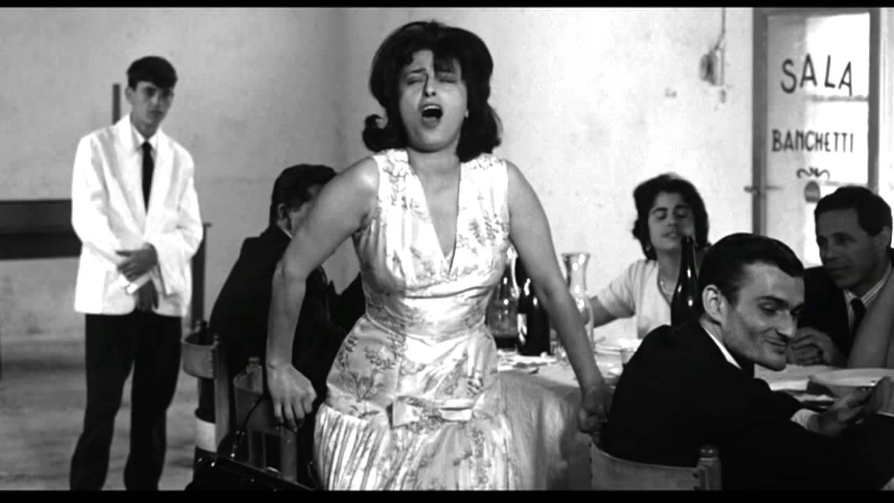     
    Il corpo performativo di Anna Magnani durante la battaglia degli stornelli in Mamma Roma di P.P. Pasolini, 1962