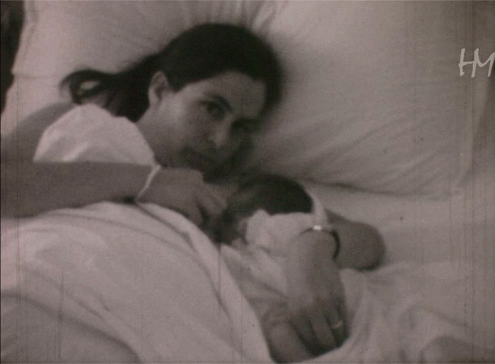 Grazia lancia un&rsquo;occhiataccia al marito che la riprende mentre cerca di allattare la figlia neonata. Giuseppe Lenzi, HMLENZGIU-0043, 8mm, 1970, conservato presso Home Movies &ndash; Archivio Nazionale del Film di Famiglia.
